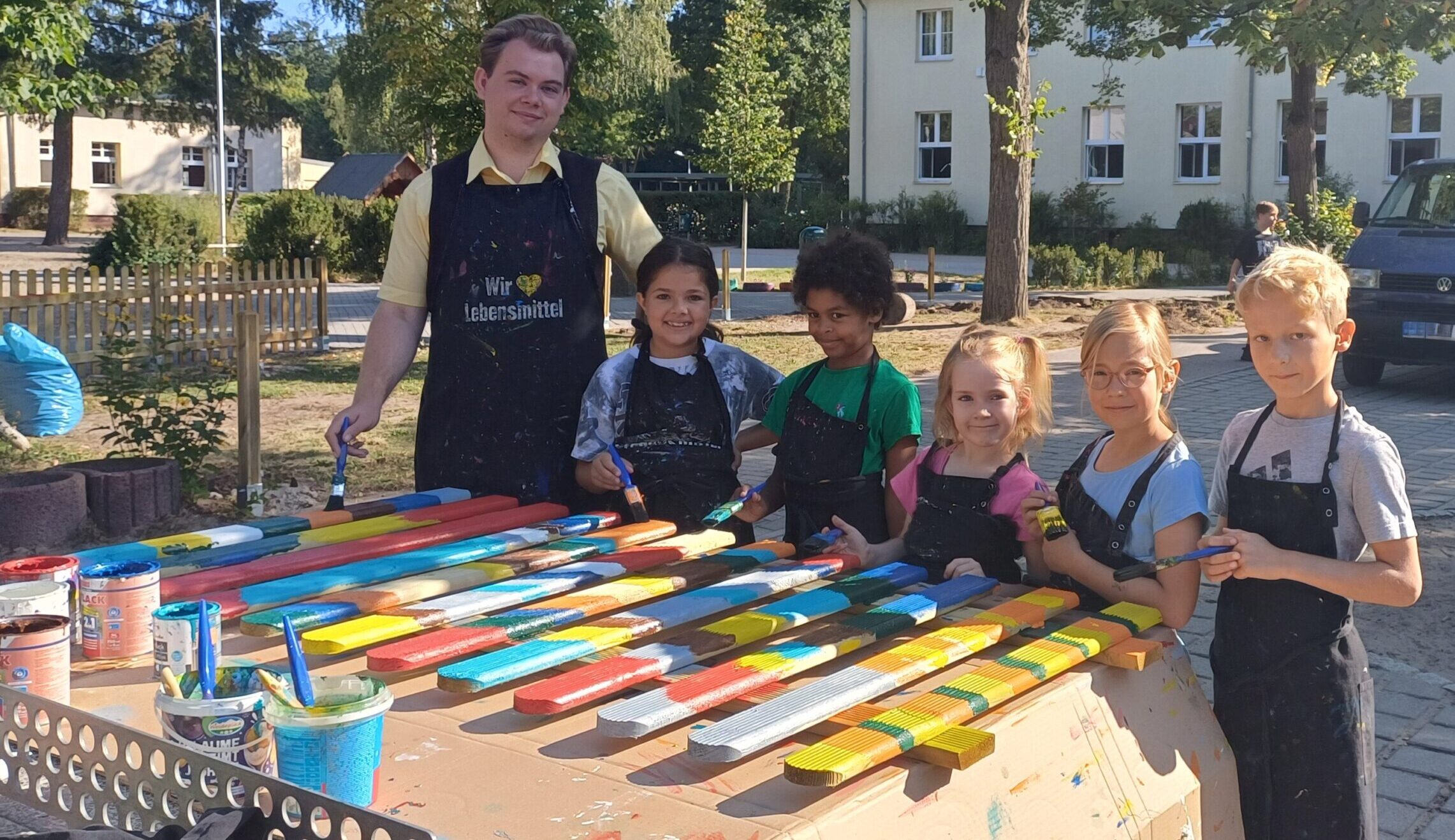 Farbklekse für den Pausenhof: Areti, Latoya, Nele, Emilia und Emil (von links) haben in der letzten Ferienwoche mit Bundesfreiwilligendienstler Dennis Maschlonkowski Zäune quietschbunt angemalt. Sie sollen helfen, dass sich die Rasenflächen etwas erholen können. Foto: Iris Maschlonkowski
