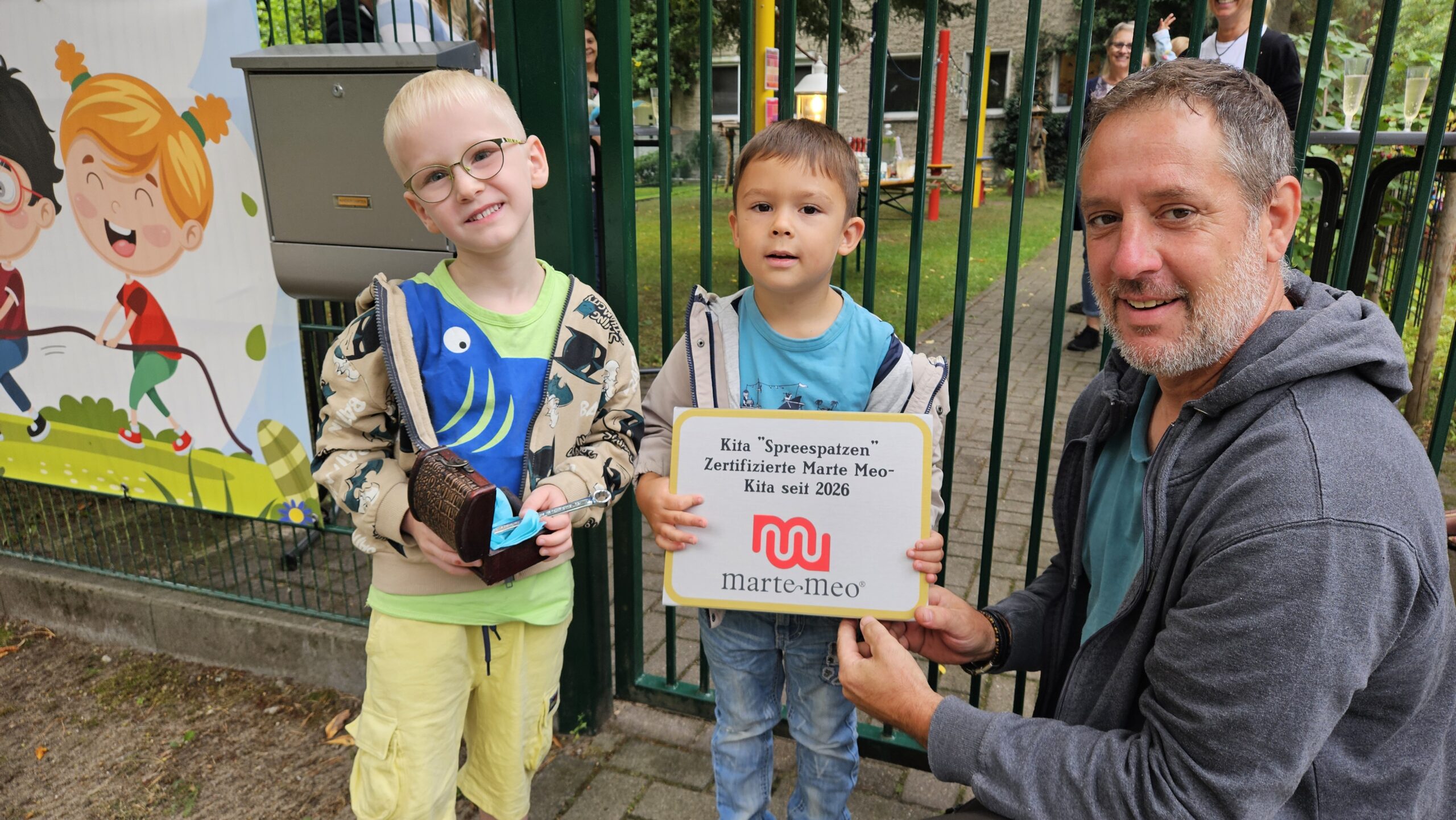 Jetzt können es alles sehen: Die Spreeauer Kita „Spreespatzen“ ist eine zertifizierte Marte Meo-Kita. Leon (5) und Leano (vier) durften Hausmeister Robert Kurzhals (von links) beim Anschrauben des Schildes helfen. Foto: Anke Beißer